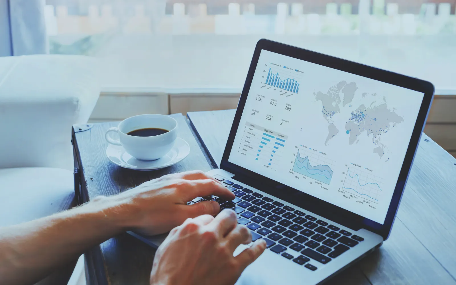 Hands typing on a laptop showing a data dashboard, with a cup of coffee on the desk