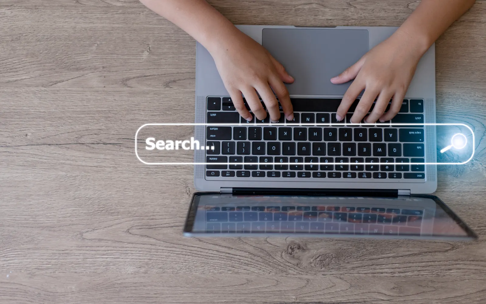 Hands typing on a laptop with a glowing search bar