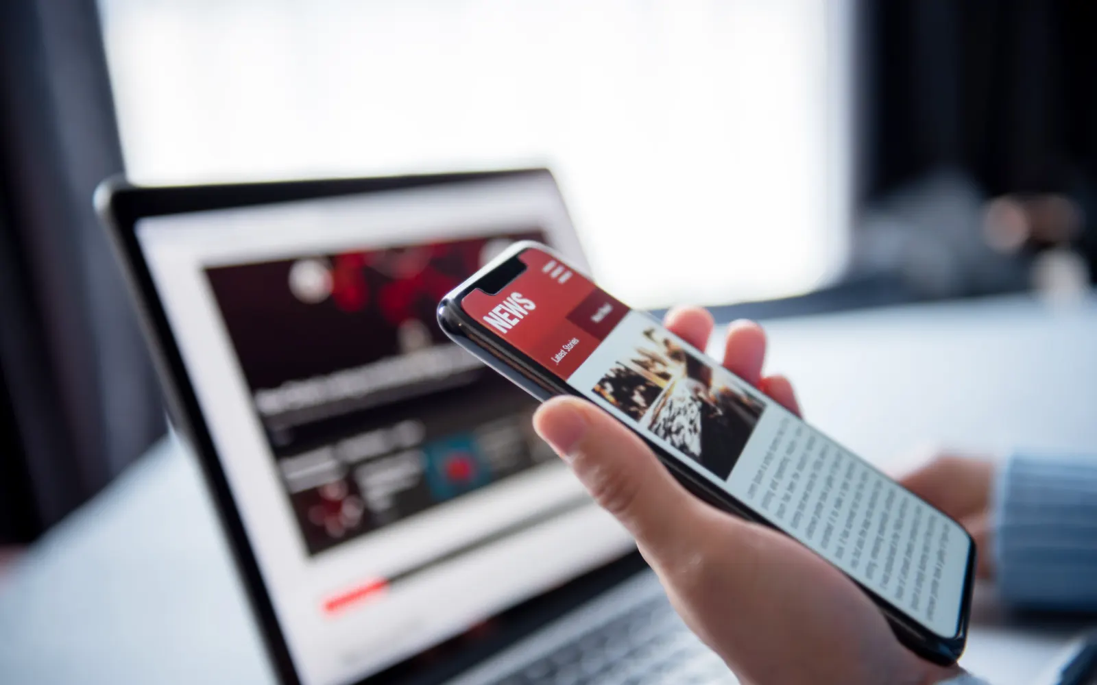 Person reading an article on a smartphone in front of a laptop