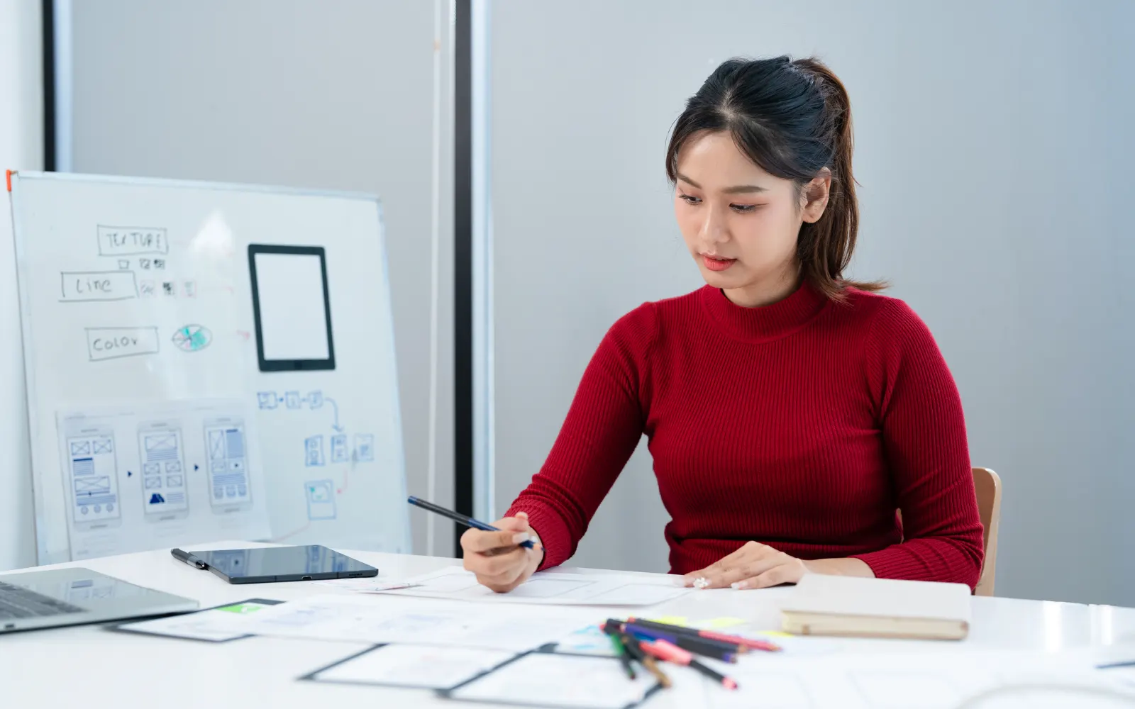 Designer sketching website wireframes at a desk beside a whiteboard