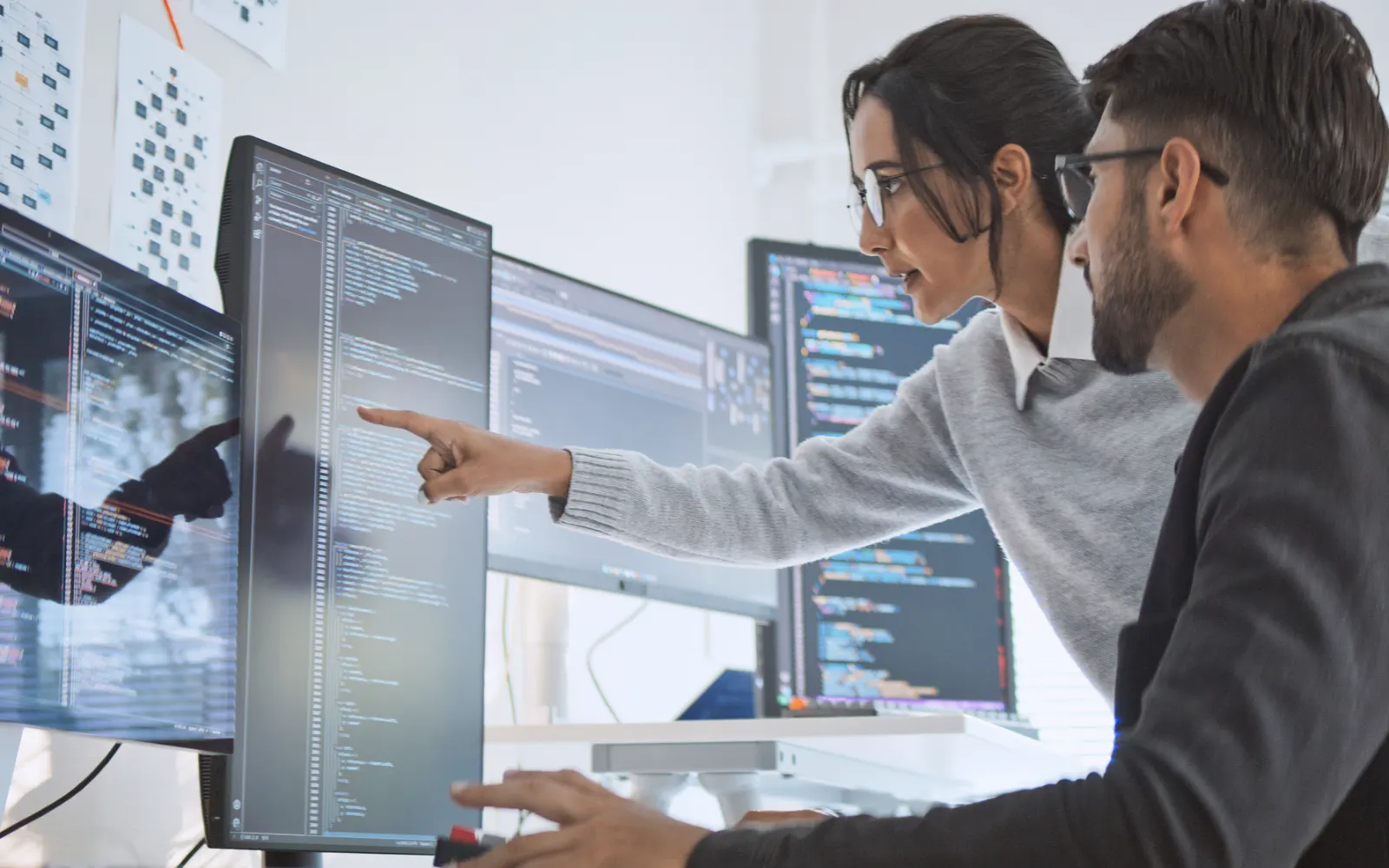 Two developers pointing at code on a large monitor