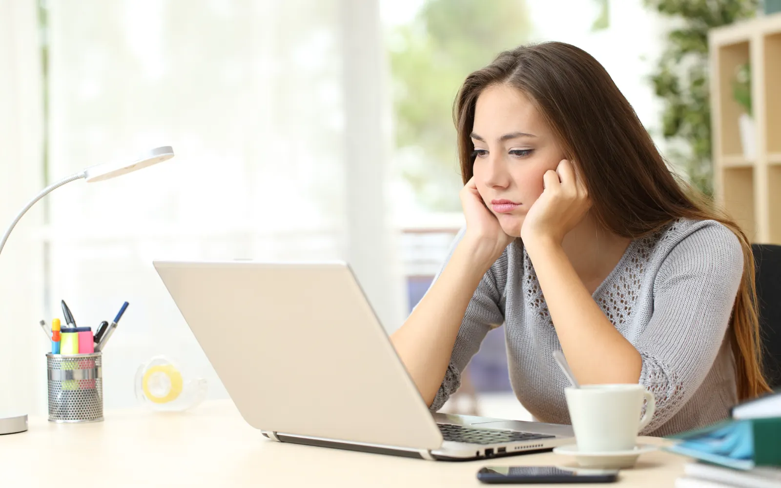 Bored woman resting her head on her hand while waiting at a laptop